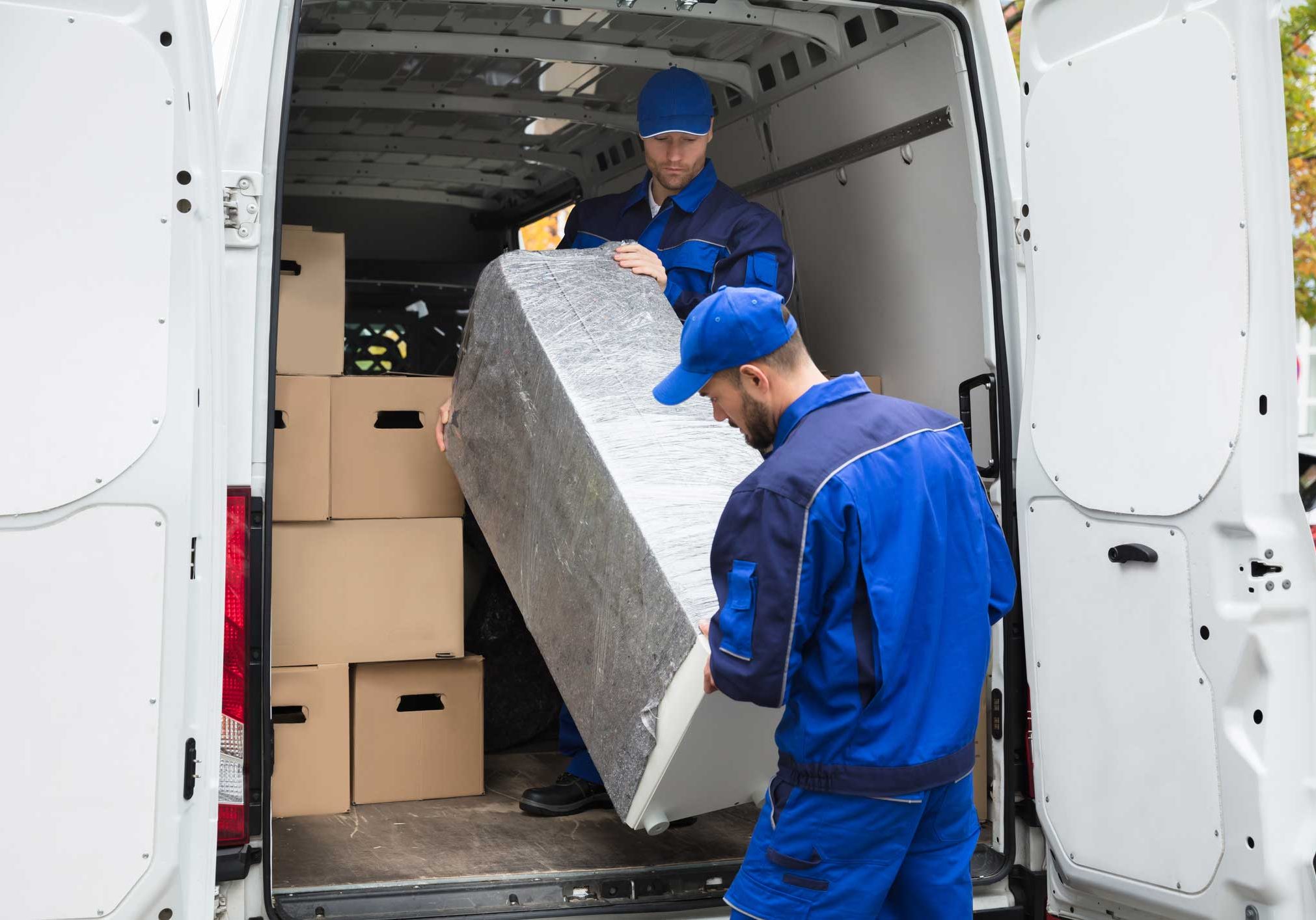 Two Delivery Men Unloading Furniture From Vehicle